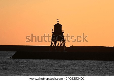 Beacon lighthouse in silhouette at sunrise on winter morning at mouth of River Tyne, North East England.
