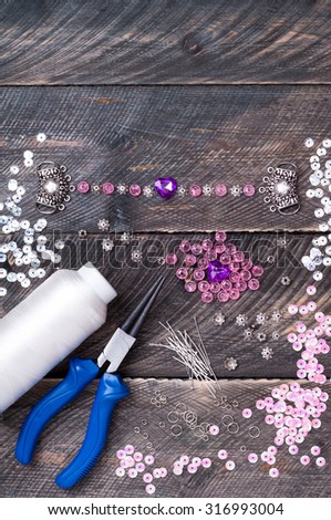 Beads, pendants, plier, glass hearts and accessories to create hand made jewelry on wooden table. Making bracelet. Top view