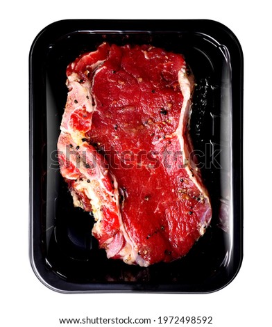 Beaf steak with bone sprinkled with pepper, on a food package tray, isolated on a white background. Entrecote with bone in MAP package, top view. Packshot photo for package design, template.