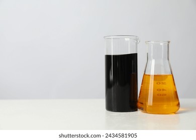 Beaker and flask with different types of oil on white table, space for text