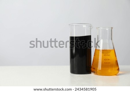 Beaker and flask with different types of oil on white table, space for text