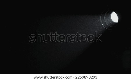 A beam of light from a spotlight illuminates a dark room. Dust particles float and sparkle in the beam of light from the lamp. Close up.