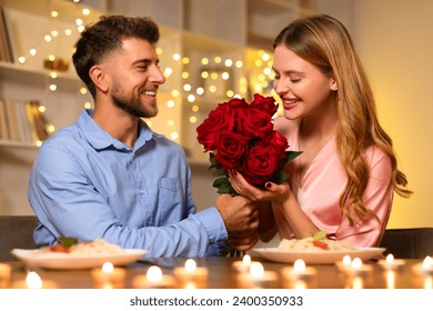 Beaming with joy, man presents a lush bouquet of red roses to a woman, adding a touch of romance to their candlelit dinner setting - Powered by Shutterstock