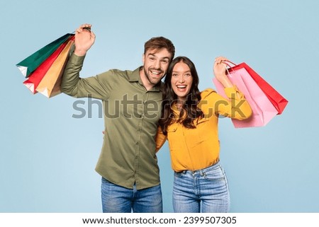 Beaming young man and woman joyfully showing off their colorful shopping bags, exuding happiness and satisfaction from their spree on a blue background