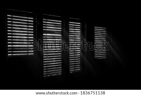 Beams of sunlight through old wooden blinds. Light coming through windows of an old abandoned house. Abstract background, black and white image. 