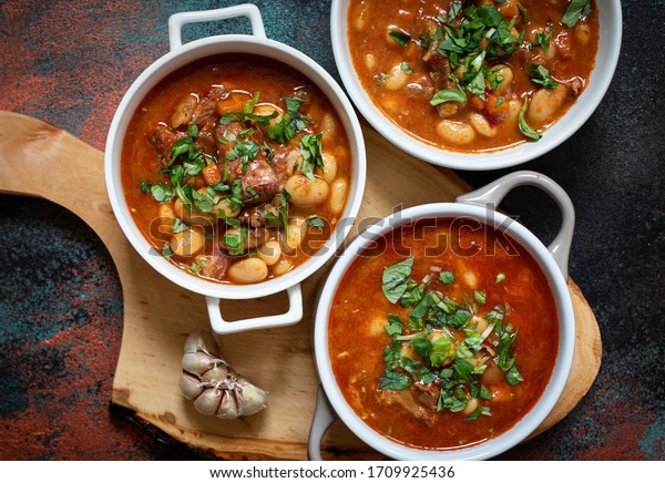 Bean soup with meat and vegetables served on a\
rustic board with garlic. Traditional Balkan soup or stew Corbast\
Pasulj (Grah). Top view, copy\
space