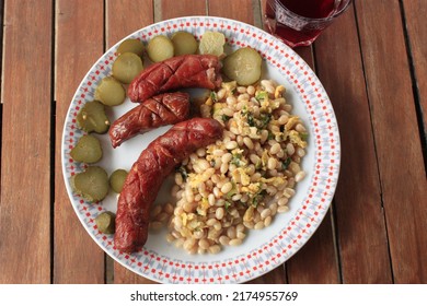 It Is Beans With Eggs And Onion. It's A Fried Sausages. It Is Pickled Cucumbers On Wheels. In The Glass Is Rasberry Tea.