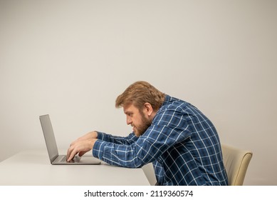 Beard emotional man in slouching position sitting in office room, working with laptop