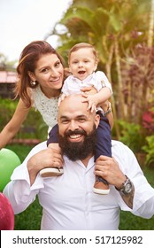 Beard Father Hold Son On Shoulder With Mother. Latino Happy Family In Summer Day