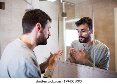 Beard Man Applying Hydrating Cream On Face In Bathroom