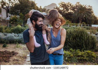 Beard Man Carrying Little Girl On Shoulder With Woman Laughing At The Farm. Beautiful Family Of Three Having Fun At Their Farm.