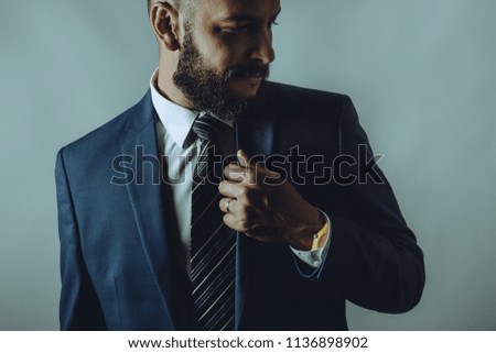 Beard man in a suit smiles while fixes tie