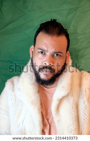 Bearded adult man with neatly trimmed hair and bling earrings on a green background