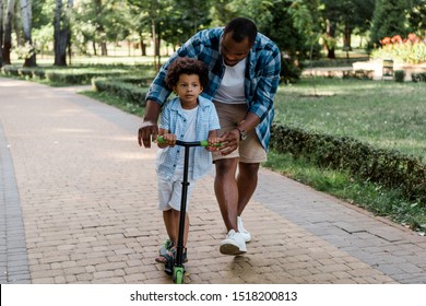 bearded african american father looking at curly son riding scooter 