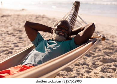 Bearded african american senior man with hands behind head lying on hammock at beach in summer. - Powered by Shutterstock