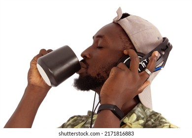 Bearded African Man Wearing A Hat With A Cup In His Hands Drinking Coffee, And Looking In Profile Listening To The Music. Addicted To Coffee Or Tea. Coffee Flavor