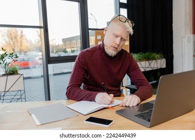 bearded albino businessman in glasses writing on notebook near gadgets on desk - Powered by Shutterstock