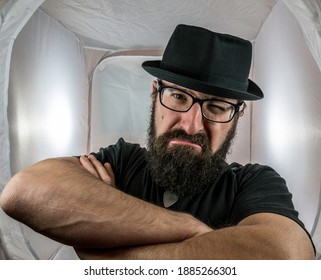 A Bearded And Angry Looking Man, Looking Like A Doorkeeper With Black Glasses And Hat