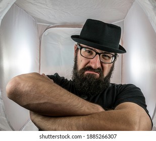 A Bearded And Angry Looking Man, Looking Like A Doorkeeper With Black Glasses And Hat