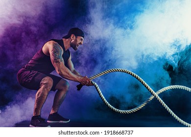 Bearded athletic looking bodybulder work out with battle rope on dark studio background with smoke. Strength and motivation. - Powered by Shutterstock