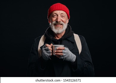 Bearded Beggar Male Smiling, Happy Even Living In Street. Cheerful Homeless Man With Mug Of Hot Tea Isolated Over Black Background