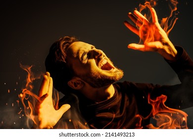 A Bearded Brunet Man Is Burning Suffering And Screaming With Pain. Studio Portrait On A Dark Background. People, Emotions.