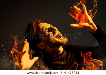 A bearded brunet man is burning suffering and screaming with pain. Studio portrait on a dark background. People, emotions.