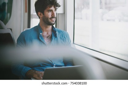 Bearded Business Man Working On A Portable Computer Connected To Public Wi-fi While Sitting In A City Bus. Young Attractive Male Is Looking At The Window While Typing Messages By A Laptop.