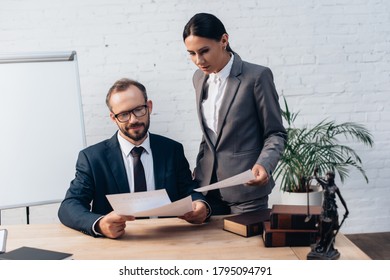 bearded businessman and brunette businesswoman looking at documents in office