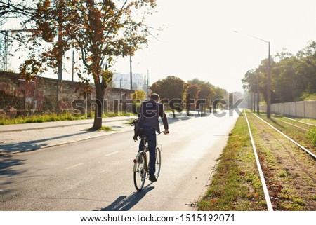 Bearded Businessman in business suit riding on retro bicycle to work on urban street in the morning on sunset