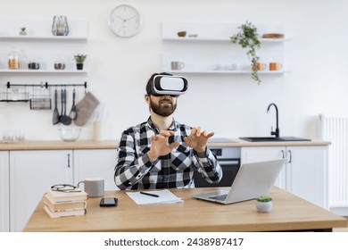 Bearded businessman making presentation using new gadget during remote working online at home. Excited Caucasian worker testing VR headset while sitting at wooden table in modern kitchen.