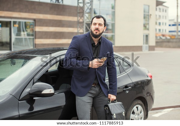 bearded businessman\
near a car with a phone