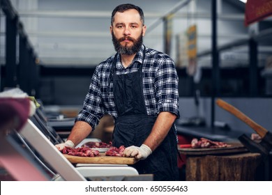Bearded Butcher Dressed In A Fleece Shirt Serving Fresh Cut Meat In A Market.