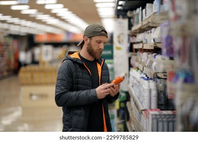 A bearded caucasian man customer is interested in a deodorant spray bottle at the grocery store, supermarket