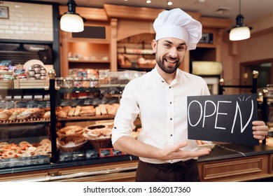 A bearded chef in a hat shows his hand on a plate openly. A large selection of excerpts in the store of fresh excerpts.