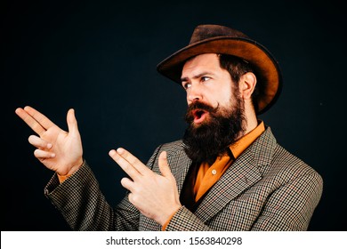 Bearded cowboy in suit and hat isolated at black background. Hipster self confident man wearing retro style suit and hat. Cool bearded gesticulative man
