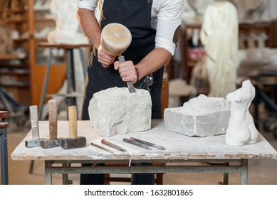 Bearded craftsman works in white stone carving with a chisel. Creative workshop with works of art.