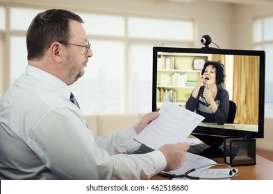 Bearded Doctor In White Shirt Carefully Checks Blood Pressure Report Of Virtual Female Patient And Looks How Mature Black Haired Woman Takes A Pill At The Same Time.