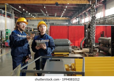 Bearded Factory Engineer In Hardhat And Safety Goggles Pointing At Chains And Explaining Coworker How To Use Industrial Crane