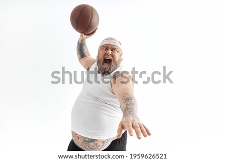 bearded fat caucasian tattoed man with basketball ball in white background. He is funny and happy 