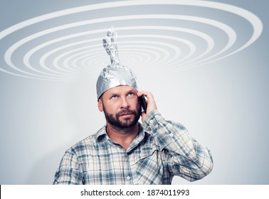 Bearded funny man in an aluminum hat talking on a smartphone with the sky, taking cosmic electric waves, concept idiots