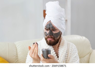 Bearded funny man having fun with a cosmetic mask on his face made from black clay. Men skin care, humor and spa at home concept
