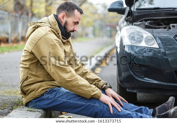Bearded guy is repairing a car on the road, a car\
broke down on a trip