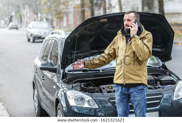 Bearded guy is repairing a car on the road, a car\
broke down on a trip