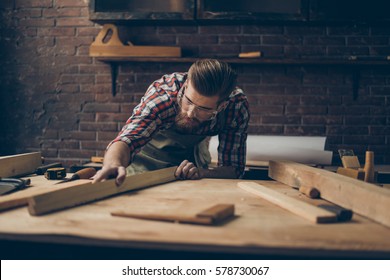 Bearded handsome cabinetmaker at the tabletop with tools.  Stylish craftsman with brutal hairstyle and saved glasses holding woodenplank at his workstation. - Powered by Shutterstock