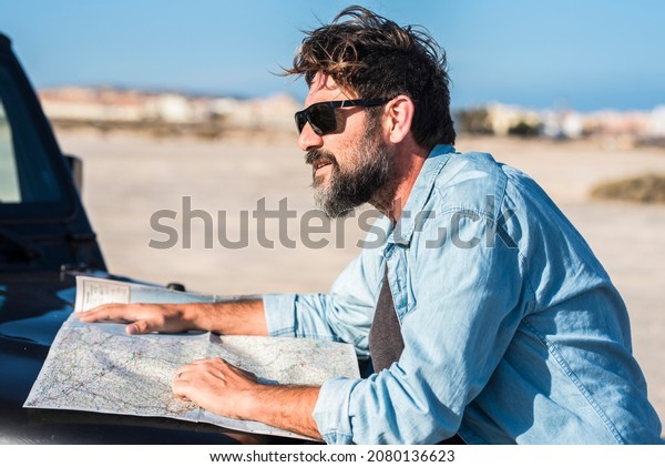 Bearded handsome man\
choose destination on paper map on the nose of his car in travel\
adventure leisure activity. Concept of road trip people and\
vehicles. Freedom and\
holidays