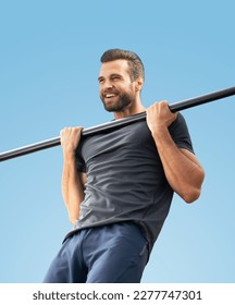 Bearded handsome man, doing pulling up exercise at horizontal bar, during workout fit training, outdoors. Fitness, sport, crossfit concept. Blue sky background.