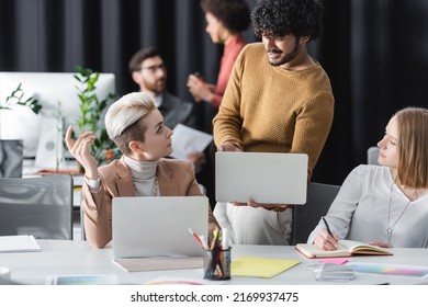 Bearded Indian Man Holding Laptop While Talking To Designers In Advertising Agency