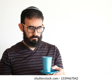 Bearded Jewish  holding a cup of wine for the Kidush on Shabbat. The man is standing in front of a white background with a serious expression
