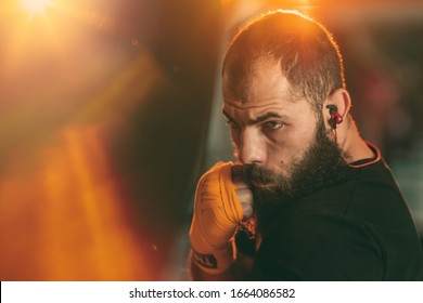 Bearded Male boxer training with punching bag in dark sports hall with sunset sunshine. - Powered by Shutterstock